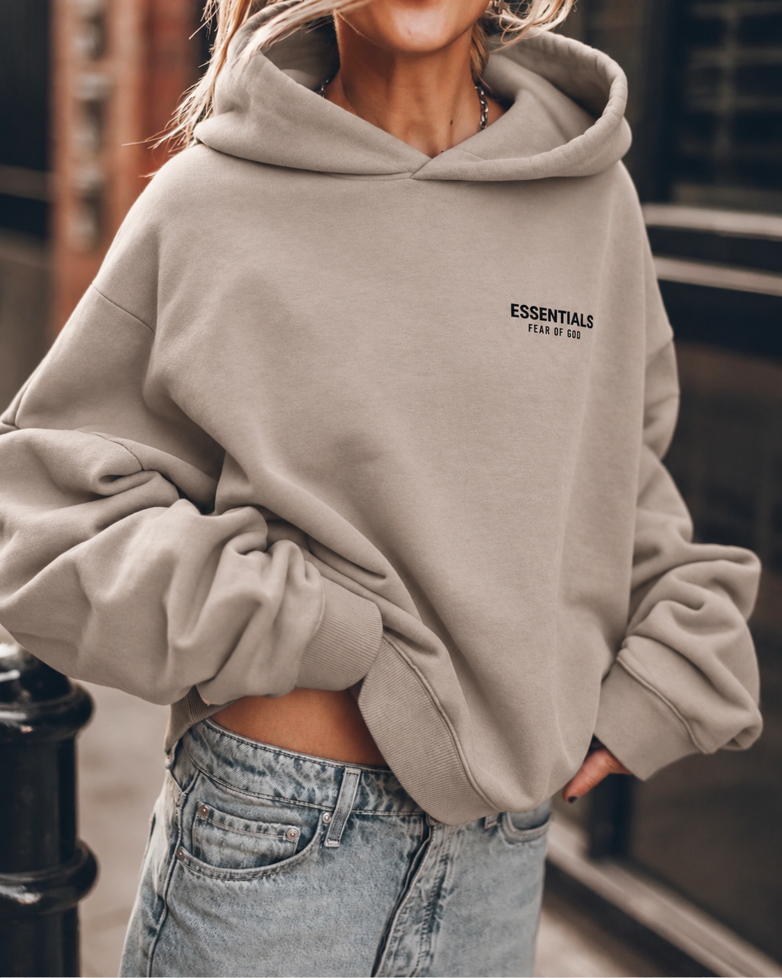 Sweat à capuche Naël sable Fear of God Essentials 192HO246257F porté avec un jean, petit logo noir sur la poitrine gauche