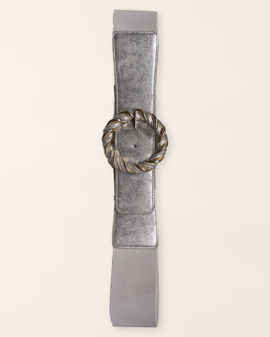 Ceinture SOLINE argentée, bande élastique et boucle ronde torsadée aux détails dorés, vue à plat sur fond beige.
